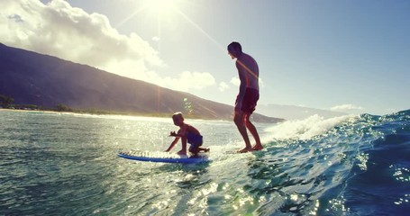 Father and son having fun surfing together at sunrise