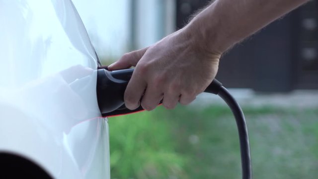 CLOSE UP: Businessman plugging in Tesla electric car at super charging station