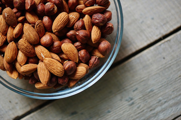 Glass bowl with almonds and hazelnuts is on a wooden table closeup