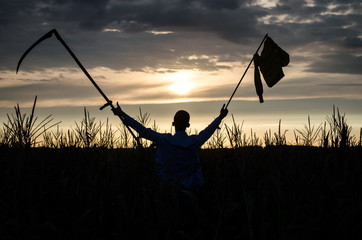 Fototapeta na wymiar silhouette at sunset of man in shorts and a t-shirt in a cornfield with hand-made yellow flag caught with hands and show the direction with hand at sky cloud background