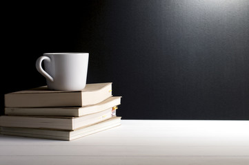 Still life - A cup of coffee put on old books on white wooden table in font of grunge black background.