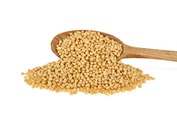 Yellow mustard seeds in wooden spoon isolated on white backgroun