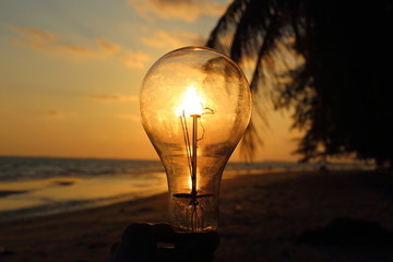 electric light bulb and sun at beach sunset sky