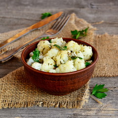 Spicy marinated cauliflower in a clay bowl, fork, knife, burlap on old wooden background
