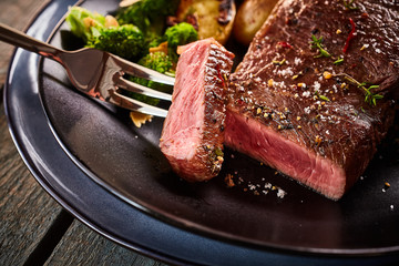 Medium rare cut of beef steak on fork in plate