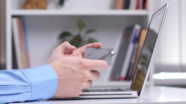 Man makes a purchase online using phone and laptop in the office. Close up
