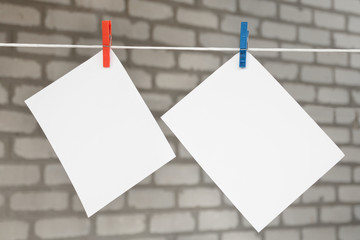 Two white blank sheets of notes with clothespins hanging on bricks background