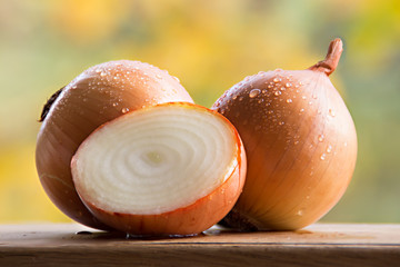 Fresh sliced and whole onion bulbs closeup. Vegetables with water drops on a wooden table. Sunny blurred background © olgabek