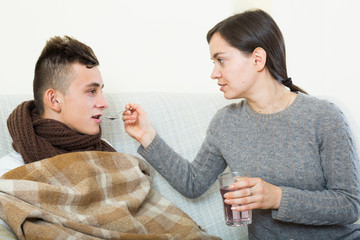 Mother treating teenage boy with syrup at home