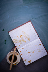 Splashes of coffee on the opened notebook. A cup of coffee, tea cup, a pencil. On dark background.