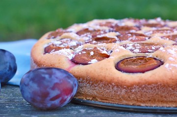 Piece of summer cake with plums on blue cloth on wooden background