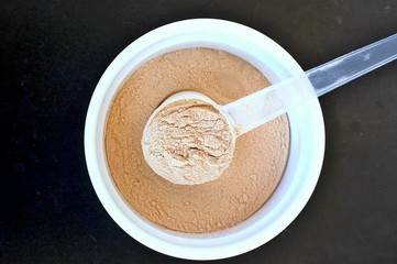 Plant protein powder from rice a pea in white bowl with plastic spoon on black background