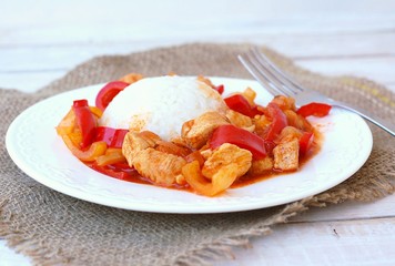 Meal from chicken meat with Indian spices, green and red pepper and rice on white plate, gunny cloth and wood with fork