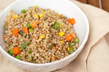 Healthy Czech vegan meal, buckwheat with carrot, sweet corn, peas, green beans and onion in white bowl with fork on the brown cloth