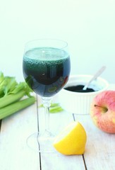 Healthy fresh smoothie drink from red apple, green algae spirulina, lemon, and celery in the glass on wooden background