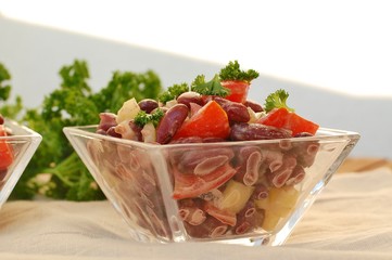 Fresh healthy vegan salad with red beans, tomato, pepper, red pepper and parsley in glass bowl on brown cloth on wooden background