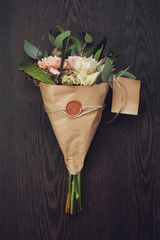 bouquet of flowers in the kraft paper on a dark wooden backgroun
