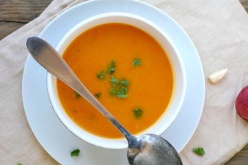 Healthy orange soup from pumpkin hokaido, green celery, garlic, onion and parsley in boxl with spoon on brown cloth and wooden background
