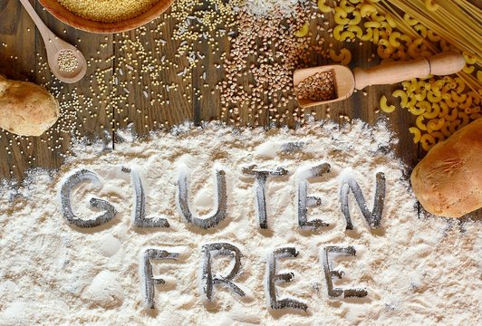 Gluten free cereals corn, rice, buckwheat, quinoa, millet, pasta and flour with text gluten free on brown wooden background