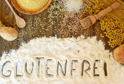 Gluten free cereals corn, rice, buckwheat, quinoa, millet, pasta and flour with text gluten free in German language on brown wooden background