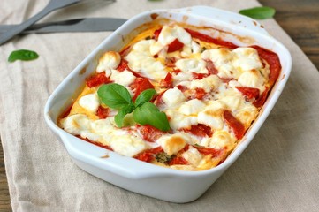 Gluten free meal from roasted corn flour, tomato, goat cheese and basil in white bowl on the cloth on brown wooden background