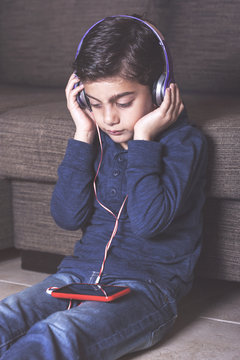 Young boy with smartphone and headphones listening to music at home