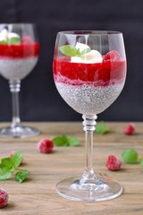 Pudding from chia seeds and raspberries with cottage with mint in glass on brown wooden background