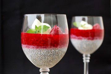 Pudding from chia seeds and raspberries with cottage with mint in glass on brown wooden background