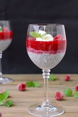 Pudding from chia seeds and raspberries with cottage with mint in glass on brown wooden background