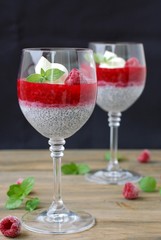 Pudding from chia seeds and raspberries with cottage with mint in glass on brown wooden background