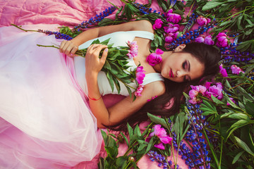 beautiful girl lying on green grass among colored flowers
