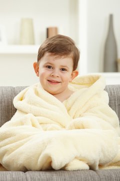 Portrait of happy kid sitting in oversize bathrobe