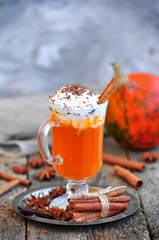 Pumpkin smoothie with cinnamon and whipped cream on a wooden background.