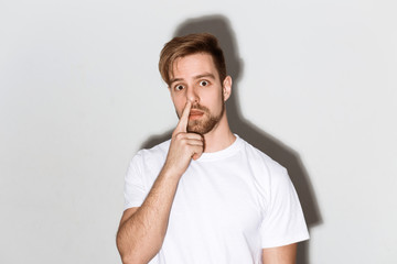 An emotional image of a young caucasian man with a beard in a white t-shirt on a bright background