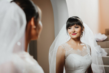 Naklejka premium Beautiful young bride with wedding makeup and hairstyle in bedroom, attractive newlywed woman have final preparation for wedding. Happy Bride waiting groom. Marriage Wedding day moment. Bride portrait