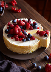 Homemade Christmas winter berry fruit cheesecake on wooden dark table. Japanese creamy mascarpone dessert. Cozy atmospheric photo.