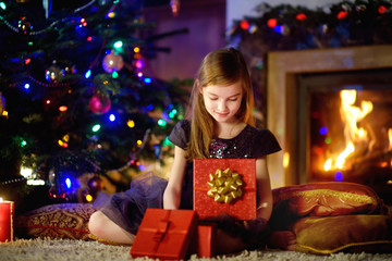 Fototapeta na wymiar Happy girl opening Christmas gifts by a fireplace