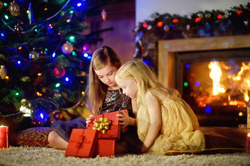 Fototapeta na wymiar Happy little sisters opening magical Christmas gift by a fireplace