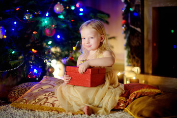 Happy girl opening Christmas gifts by a fireplace