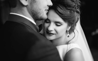 Happy beautiful bride and elegant stylish groom have buried against each other with their eyes closed. Close-up. Romantic concept. Black and white