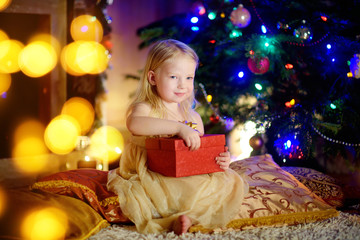 Obraz na płótnie Canvas Happy girl opening Christmas gifts by a fireplace