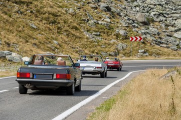 Three old cabriolet cars travel over the high mountain.
