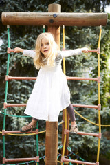 Portrait of Happy little blond girl playing on a rope web playground outdoor

