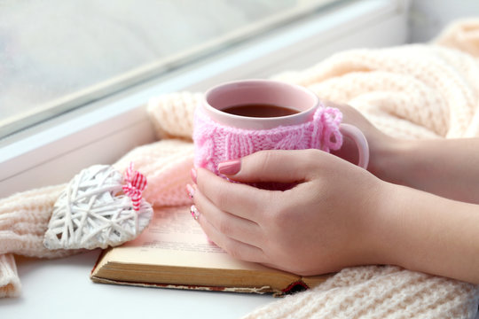 Woman hands holding cup of coffee near the window
