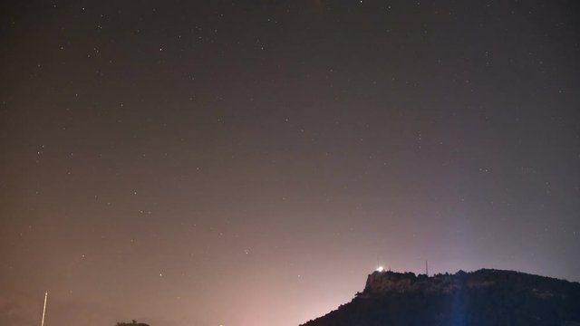 night timelapse of hill with the stars on the sky and colourful lights below