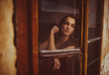 Strong woman sits thoughtful behind an old window