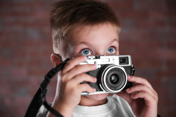 Little boy with vintage camera on brick wall background