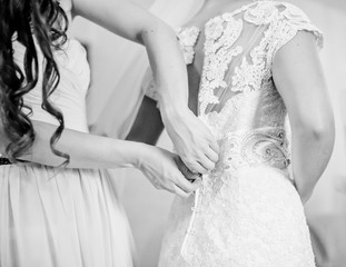 Fototapeta na wymiar Bridesmaid buttons up a corset on delicate bride