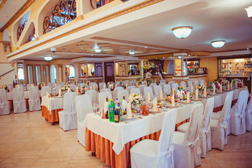 Long dinner tables covered with orange cloth stand in the restau