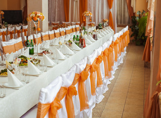 White chairs decorated with orange ribbons stand at the long din